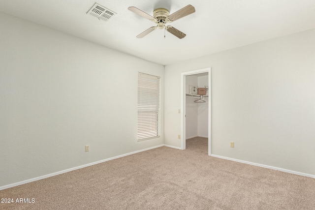 unfurnished bedroom featuring light colored carpet, ceiling fan, a closet, and a walk in closet