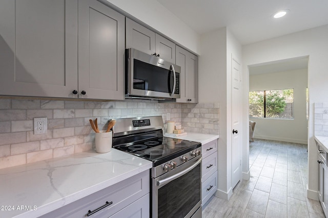 kitchen featuring gray cabinetry, light stone countertops, backsplash, light hardwood / wood-style floors, and stainless steel appliances