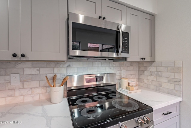 kitchen with gray cabinets, tasteful backsplash, stainless steel appliances, and light stone counters