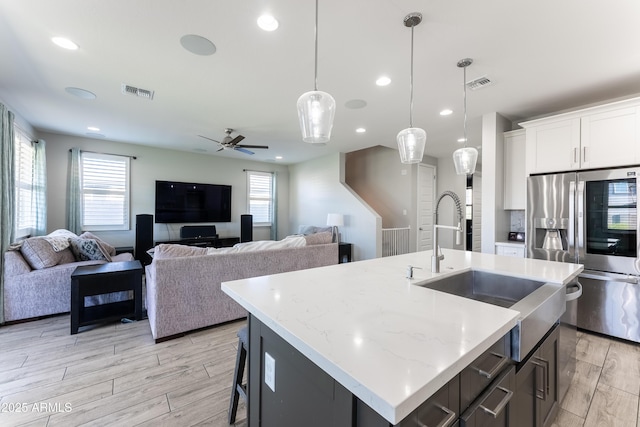 kitchen with stainless steel refrigerator with ice dispenser, ceiling fan, a kitchen island with sink, hanging light fixtures, and white cabinets