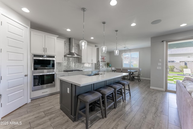 kitchen featuring stainless steel appliances, decorative light fixtures, wall chimney range hood, white cabinets, and sink