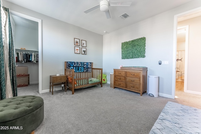 bedroom featuring ceiling fan, light colored carpet, a crib, ensuite bath, and a closet