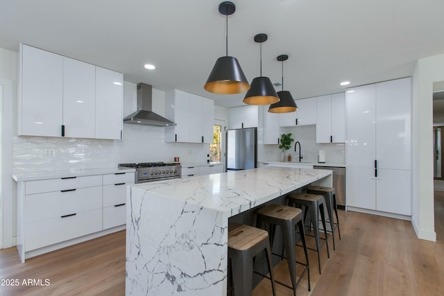 kitchen featuring stainless steel appliances, a kitchen island, wall chimney range hood, a sink, and modern cabinets