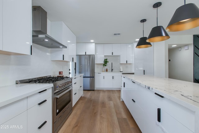 kitchen with stainless steel appliances, wall chimney range hood, modern cabinets, and visible vents