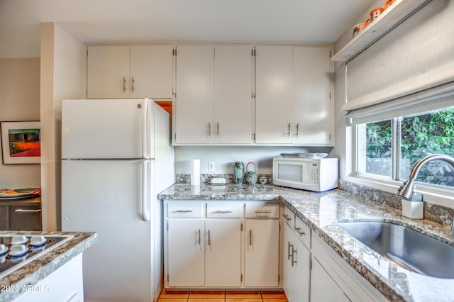 kitchen with sink, white cabinets, light tile patterned floors, light stone counters, and white appliances