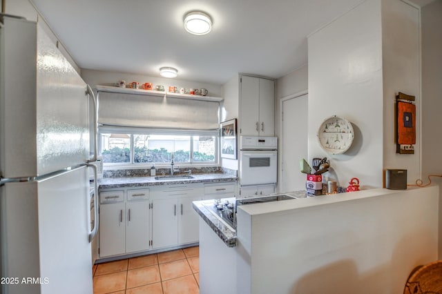 kitchen with white cabinetry, white refrigerator, kitchen peninsula, and light tile patterned flooring