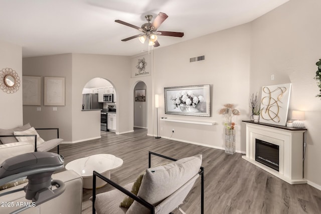 7826 W Mcrae Way, Glendale, AZ 85308 - living room with arched walkways, a ceiling fan, a glass covered fireplace, dark wood-style flooring, and baseboards