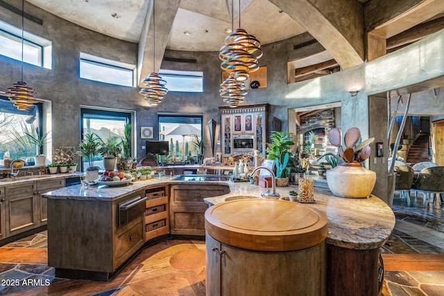 kitchen with black cooktop, sink, a kitchen island with sink, and dark stone countertops