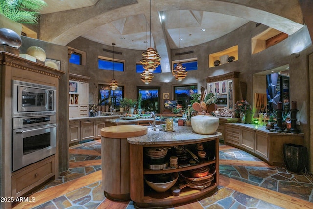 kitchen with pendant lighting, appliances with stainless steel finishes, a center island with sink, and a high ceiling