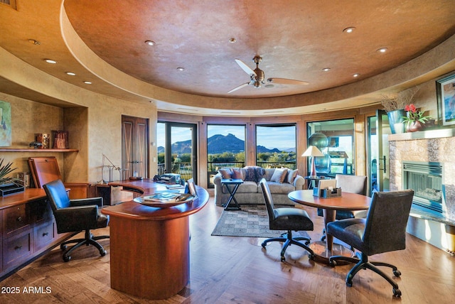 office area with a mountain view, hardwood / wood-style flooring, a raised ceiling, and ceiling fan