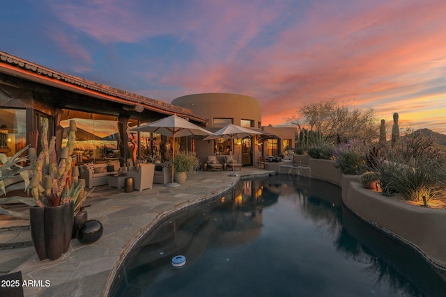 pool at dusk with outdoor lounge area and a patio