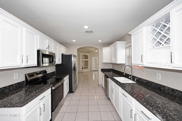 kitchen with dark stone counters, stainless steel appliances, sink, white cabinets, and light tile patterned flooring