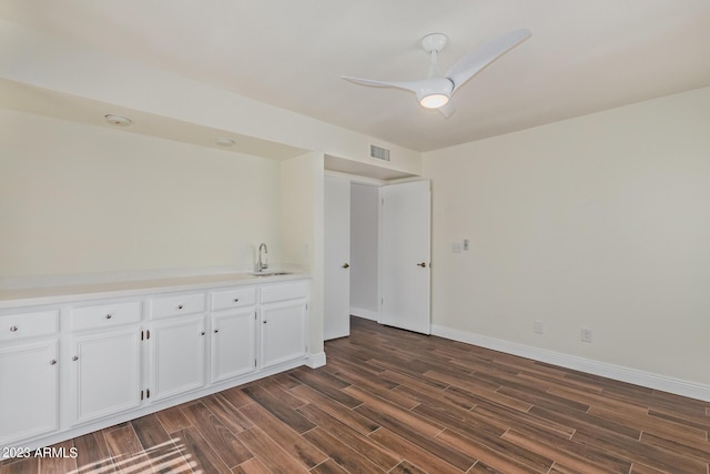 empty room featuring a sink, dark wood-style flooring, ceiling fan, visible vents, and baseboards