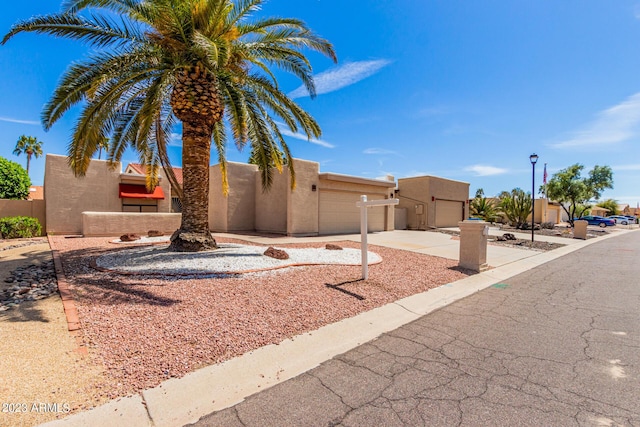 pueblo revival-style home featuring stucco siding, concrete driveway, and an attached garage