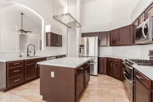 kitchen with sink, appliances with stainless steel finishes, a kitchen island, ceiling fan, and a high ceiling