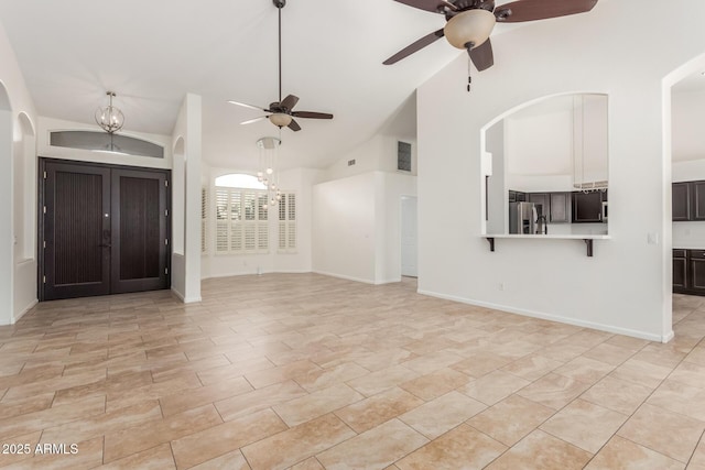 unfurnished living room featuring ceiling fan with notable chandelier and high vaulted ceiling