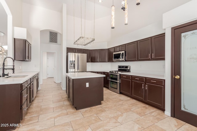 kitchen with sink, a center island, hanging light fixtures, appliances with stainless steel finishes, and a towering ceiling