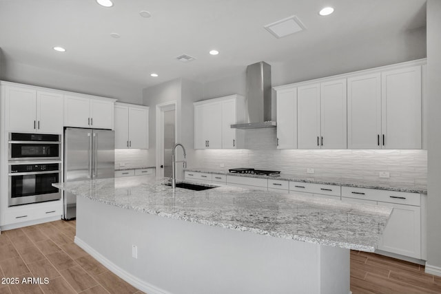 kitchen with white cabinetry, appliances with stainless steel finishes, sink, and wall chimney range hood