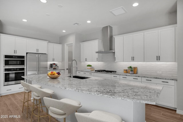 kitchen with white cabinetry, wall chimney exhaust hood, a kitchen breakfast bar, and sink