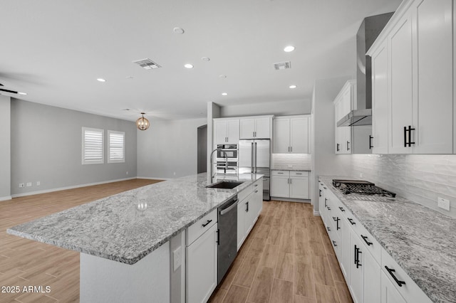 kitchen featuring sink, stainless steel appliances, light stone countertops, white cabinets, and a large island with sink