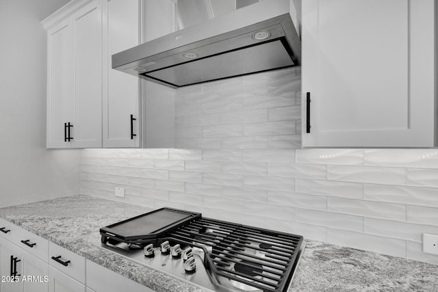 kitchen with stainless steel gas cooktop, white cabinetry, light stone counters, wall chimney range hood, and backsplash