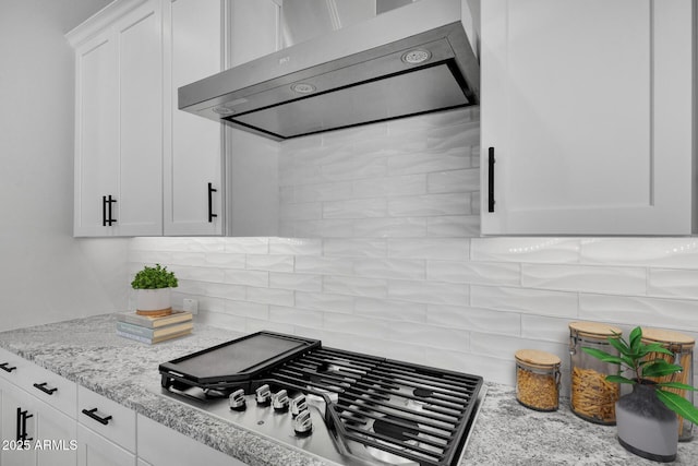 kitchen featuring wall chimney range hood, white cabinetry, light stone countertops, decorative backsplash, and stainless steel gas stovetop