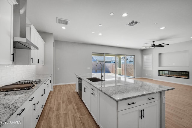 kitchen with appliances with stainless steel finishes, sink, white cabinets, light stone countertops, and wall chimney exhaust hood