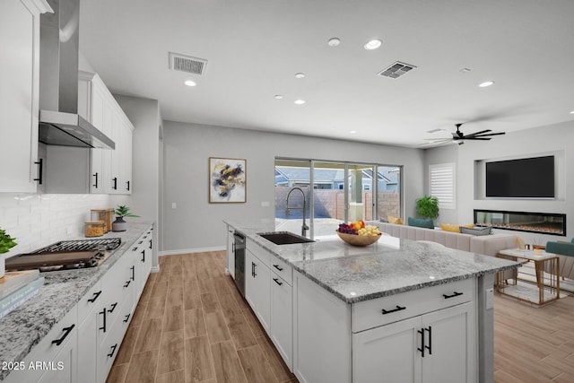 kitchen with sink, white cabinetry, light stone counters, appliances with stainless steel finishes, and wall chimney range hood