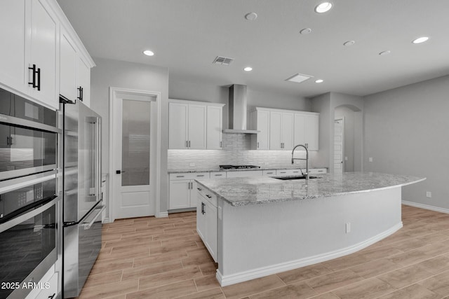 kitchen with a kitchen island with sink, sink, stainless steel appliances, and wall chimney exhaust hood