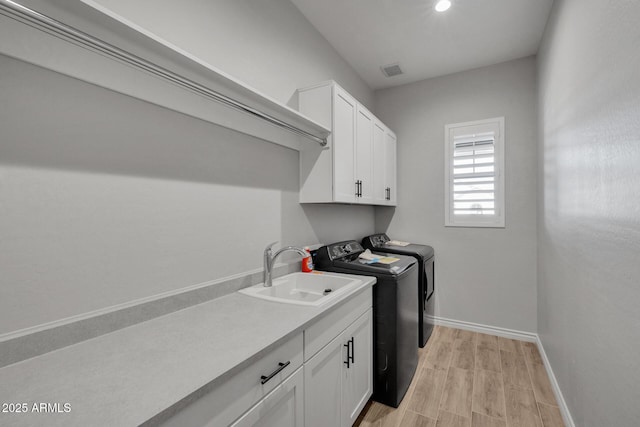 laundry room featuring light hardwood / wood-style floors, sink, washing machine and dryer, and cabinets