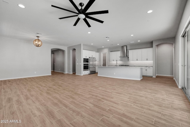 unfurnished living room with sink, ceiling fan with notable chandelier, and light hardwood / wood-style flooring