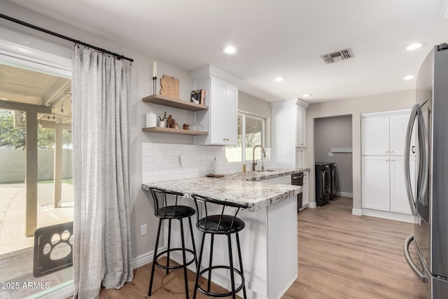 kitchen with sink, white cabinetry, stainless steel refrigerator, light stone counters, and washing machine and dryer