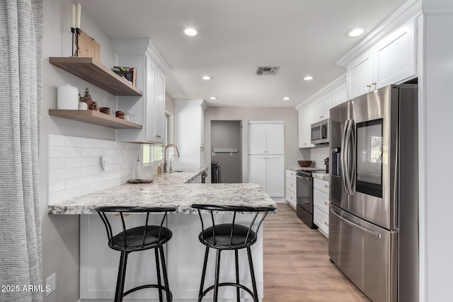 kitchen featuring a breakfast bar area, white cabinetry, kitchen peninsula, light wood-type flooring, and appliances with stainless steel finishes