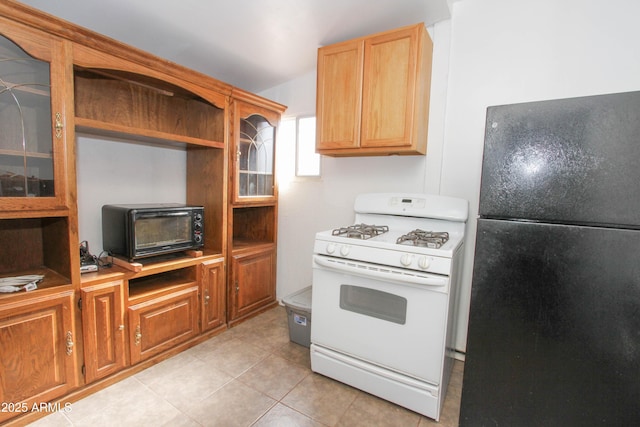 kitchen with glass insert cabinets, freestanding refrigerator, white range with gas stovetop, and light tile patterned floors