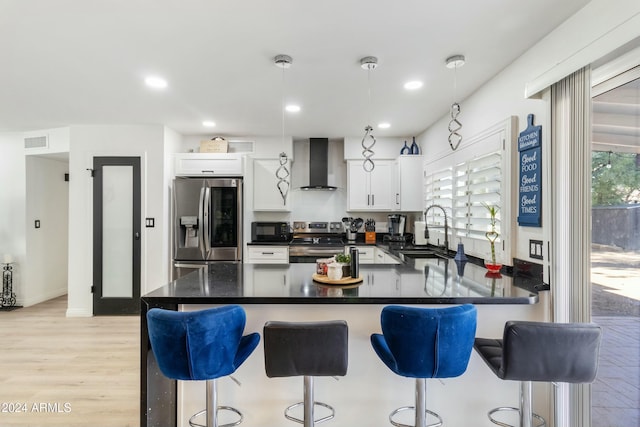 kitchen featuring white cabinetry, sink, hanging light fixtures, stainless steel appliances, and wall chimney range hood