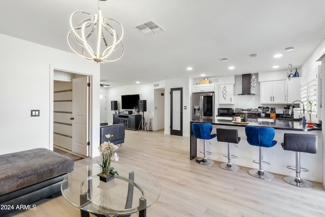 kitchen featuring wall chimney range hood, light hardwood / wood-style flooring, stainless steel refrigerator with ice dispenser, pendant lighting, and white cabinets