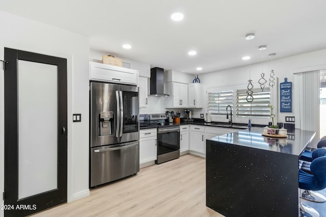 kitchen featuring stainless steel appliances, sink, wall chimney range hood, white cabinets, and hanging light fixtures