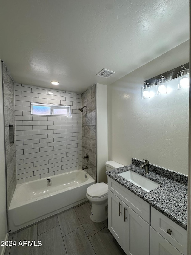 full bathroom featuring vanity, a textured ceiling, tiled shower / bath combo, and toilet