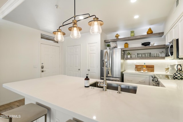 kitchen featuring a kitchen bar, decorative light fixtures, appliances with stainless steel finishes, kitchen peninsula, and white cabinets