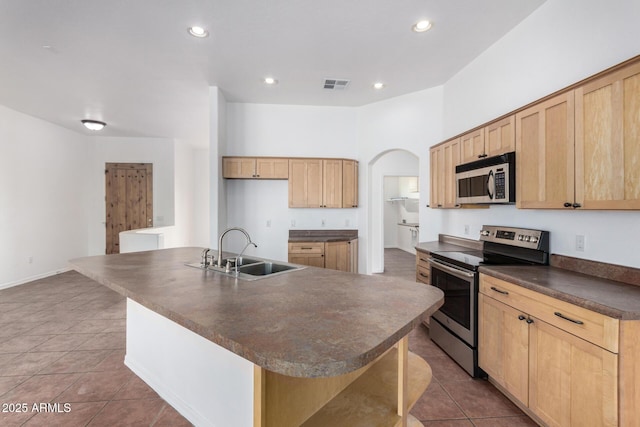 kitchen with light brown cabinetry, visible vents, dark countertops, a sink, and stainless steel appliances