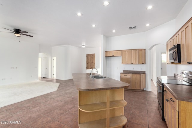 kitchen with dark countertops, appliances with stainless steel finishes, arched walkways, and a sink