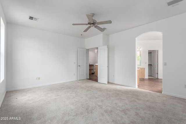 unfurnished bedroom featuring arched walkways, connected bathroom, visible vents, and carpet floors