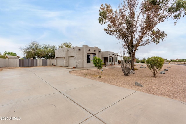 pueblo-style home featuring a garage, concrete driveway, fence, stucco siding, and a gate
