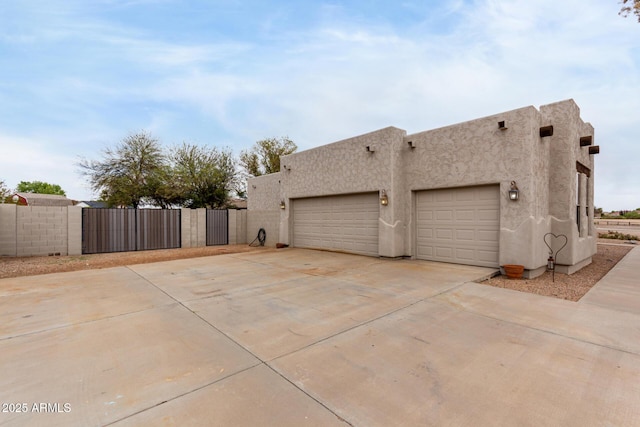view of property exterior with an attached garage, fence, stucco siding, a gate, and driveway