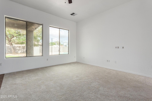 carpeted spare room featuring baseboards, a ceiling fan, and visible vents