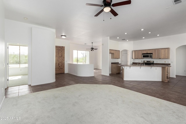 unfurnished living room with visible vents, dark colored carpet, arched walkways, dark tile patterned floors, and a ceiling fan
