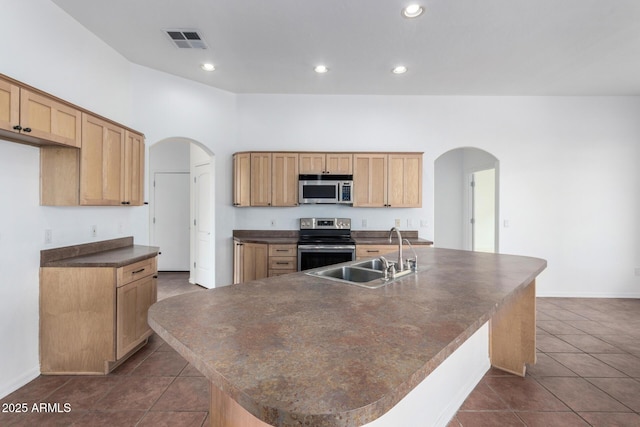 kitchen with arched walkways, dark countertops, a sink, and appliances with stainless steel finishes
