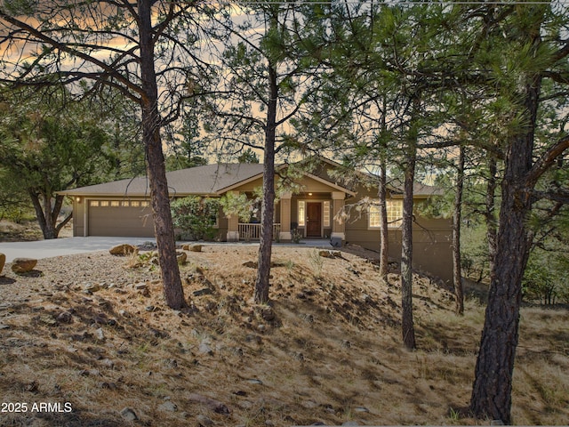 view of front of property with a garage, concrete driveway, covered porch, and roof with shingles