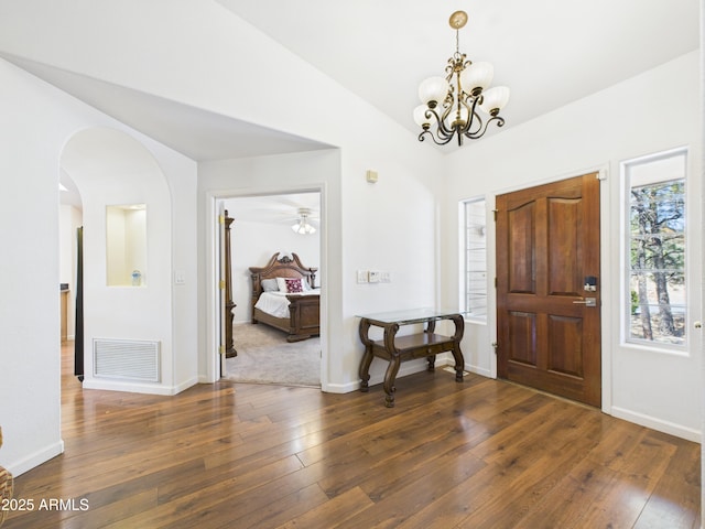 foyer with arched walkways, vaulted ceiling, dark wood finished floors, a chandelier, and baseboards
