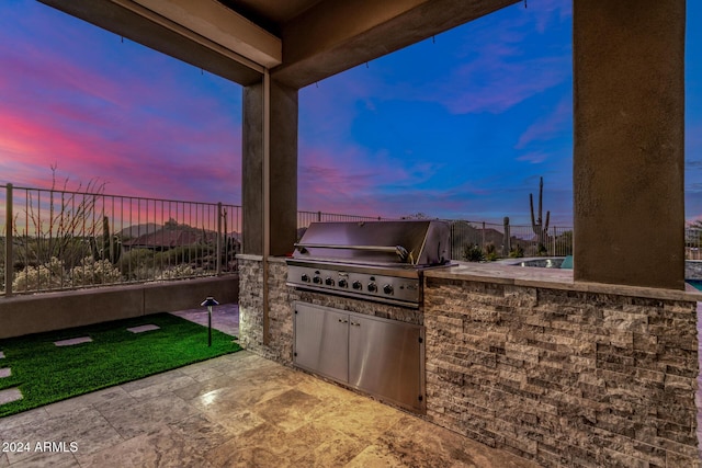 patio terrace at dusk with a grill and exterior kitchen